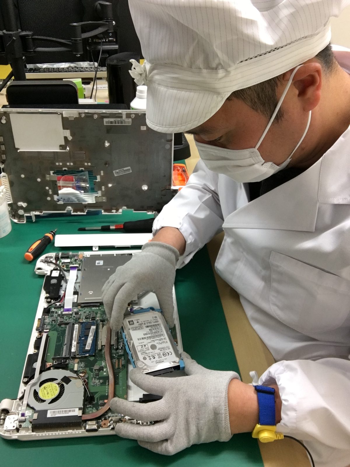 静電気対策の白衣と手袋で、ノートパソコンのハードディスクを取り外す技術者